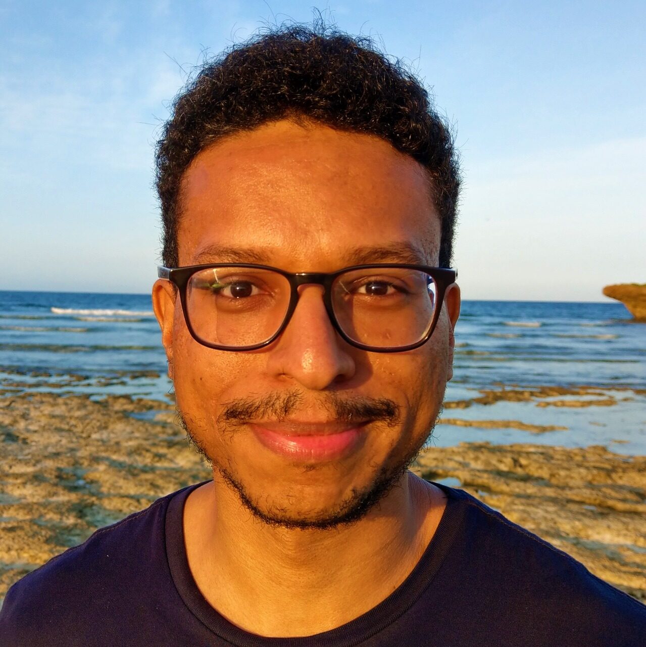 A man dressed in a black t-shirt smiles and gazes into the camera.